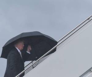 Trump sostiene un amplio paraguas mientras sube al avión oficial. Fotos AFP