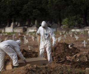 Trabajadores de un cementerio con trajes de protección colocan el ataúd de Paulo Jose da Silva, de 57 años, que murió por el nuevo coronavirus, en Río de Janeiro. Foto: AP.
