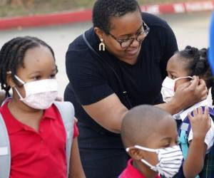 Leandra Walker, al centro, ayuda a su hija Mila Walker, de 5 años, a ponerse su mascarilla antes de que entre a la escuela con sus hermanos Olivia, de 7 años, izquierda, y su mellizo Max para el primer día de clases, el martes 17 de agosto de 2021, en Richardson, Texas. (AP Foto/LM Otero)