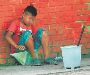Sentado en un objeto plástico, el pequeño Denis espera que el semáforo cambie de color para ofrecer sus servicios de limpiar vidrios (Foto: Alex Pérez/EL HERALDO)