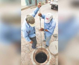 Dos empleados revisan la profundidad de una alcantarilla obstruida