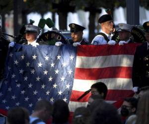 Policías y bomberos de Nueva York sostienen una bandera estadounidense mientras una banda toca el himno nacional en el monumento nacional conmemorativo del 11 de septiembre, durante la ceremonia del 20º aniversario de los atentados del 11-S en el World Trade Center, en Nueva York. Foto: AP