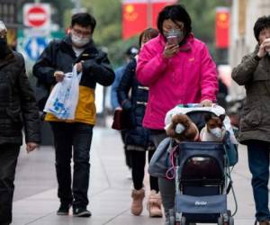 Una mujer pasea a sus perros protegidos con mascarillas en Shanghai. Foto AFP