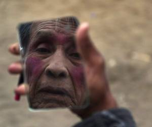 El payaso de circo Santos Chiroque, cuyo nombre artístico es 'Piojito', se mira en un espejo mientras demuestra cómo se pone su maquillaje de payaso usando sólo lápiz labial, afuera de su casa en las afueras de Lima, Perú. Foto: Agencia AP.