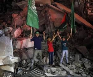 Niños palestinos ondean la bandera verde de Hamas y la palestina sobre los escombros de un edificio derribado mientras celebran el acuerdo de alto el fuego entre Israel y el grupo insurgente, en la Ciudad de Gaza. Foto:AP