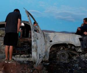 Los miembros de la familia LeBarón miran el auto quemado, donde parte de los nueve miembros de la familia fueron asesinados y quemados durante una emboscada.