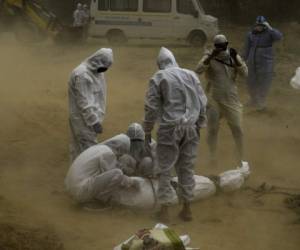 Los familiares que usan equipo de protección atan el cadáver de una víctima que murió por el coronavirus. Foto: Agencia AFP.