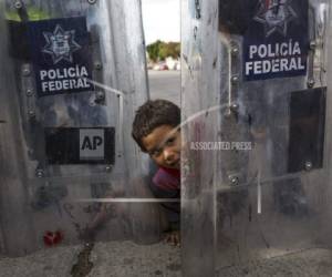 Elías López, un migrante hondureño de tres años, juega entre los escudos de la policía mexicana antimotines cuando el grupo del cual es parte intentó cruzar el cruce fronterizo Chaparral en Tijuana, México. (Foto: AP)