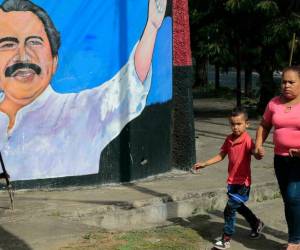 Una mujer y niños caminan junto a un mural que representa al presidente de Nicaragua, Daniel Ortega, en Managua el 10 de enero de 2022, día en que inicia su cuarto mandato.
