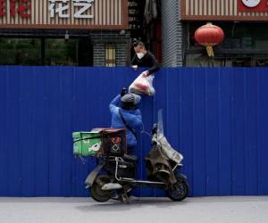 En esta foto de archivo tomada el 11 de mayo de 2022, un repartidor pasa artículos a un hombre dentro de un área residencial cercada bajo un bloqueo de coronavirus Covid-19 en Beijing.
