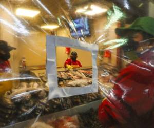 Vendedores de pescado con mascarillas protectoras atienden detrás de una lámina de plástico que cuelga sobre su mostrador en el mercado de La Vega en Santiago, Chile, en medio de la pandemia del nuevo coronavirus. Foto: AP.