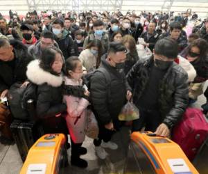 Viajeros equipados con máscaras hacen fila ante los tornos para acceder a una estación de tren en Nantong, en la provincia oriental de Jiangsu, en China, el 22 de enero de 2020. (Chinatopix vía AP)