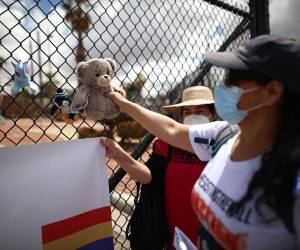 Fotografía de archivo de una mujer que cuelga de manera simbólica un muñeco de peluche como manera de representar la inocencia de los niños migrantes en las rejas de entrada de la base militar de Fort Bliss en El Paso, Texas.