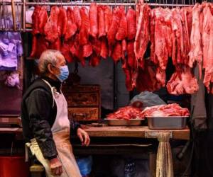 Un carnicero se sienta junto a la carne fresca que cuelga en exhibición mientras espera a los clientes en su tienda al lado de la calle en Hong Kong el 18 de enero de 2021. Foto: AFP