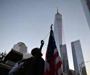 Un hombre sostiene una bandera estadounidense frente a la 'Freedom Tower' (C, trasera) durante la ceremonia de conmemoración del vigésimo aniversario de los ataques del 11 de septiembre en el World Trade Center, en Nueva York. Foto:AFP