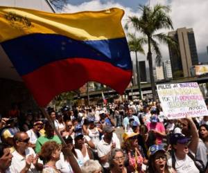 Los partidarios del líder de la oposición venezolana y autoproclamado presidente en funciones, Juan Guaido, se manifiestan con una bandera nacional venezolana y un cartel que dice 'Miles de mujeres organizadas por la democracia, luces en el apagón'. Foto AFP