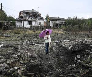 Una mujer se para frente a una casa destruida en medio de la invasión rusa de Ucrania.