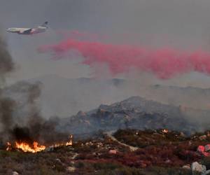 Avión de los bomberos arroja retardante de fuego sobre una ladera en llamas cerca de casas en Hemet, California.