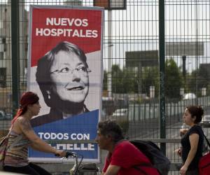 People walk past a banner with electoral propaganda of Chilean presidential candidate for the New Majority coalition, Michelle Bachelet, in Santiago, on December 11, 2013. Chile will hold the run-off presidential election on December 15, for which former Chilean socialist president (2006-2010) Michelle Bachelet is the favorite. Advocating change, she is running against right-wing candidate Evelyn Matthei. AFP PHOTO / MARTIN BERNETTI