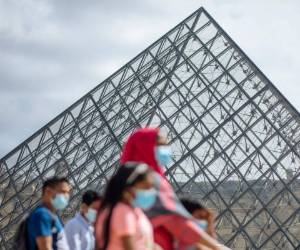 Una familia que usa mascarillas camina frente al museo Louvre en París, el sábado 15 de agosto de 2020.
