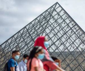 Una familia que usa mascarillas camina frente al museo Louvre en París, el sábado 15 de agosto de 2020.