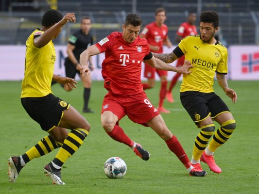 El delantero polaco del Bayern Múnich Robert Lewandowski (C) y el centrocampista inglés del Dortmund Jadon Sancho (R) compiten por el balón durante el partido de fútbol de la primera división alemana de la Bundesliga BVB Borussia Dortmund v FC Bayern Munich el 26 de mayo de 2020 en Dortmund, Alemania occidental. Foto: Agencia AFP.