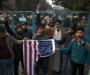 Los manifestantes sostienen una bandera estadounidense quemada. Foto AFP