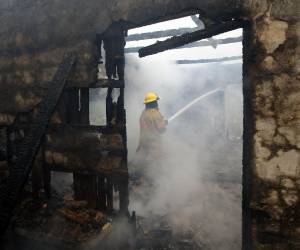 Un bombero realiza labores de extinción del incendio en las paredes de bahareque de la vivienda.