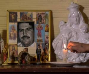 Una de sus vecinas enciende una vela frente a una retratera con la foto del fallecido capo mexicano. Foto: AFP