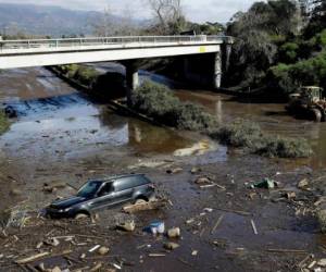 Una excavadora mueve escombros cuando un vehículo se quedó varado en agua inundada en la carretera 101 de los Estados Unidos en Montecito, California. Foto: AP