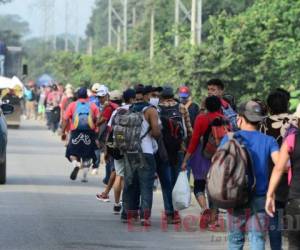 El grupo camina por una vía lateral de la carretera con la mochila al hombro, unos pocos con la bandera de Honduras y la mayoría con mascarilla por la pandemia. Fotos: AFP.