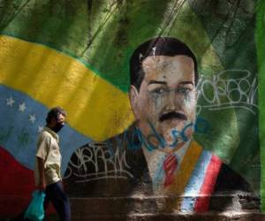 Un individuo con mascarilla pasa frente a un mural del presidente Nicolás Maduro en Caracas el 22 de julio del 2020. Foto: AP