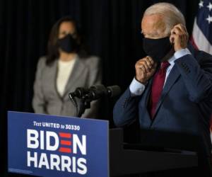 El candidato presidencial demócrata Joe Biden se coloca su mascarilla tras hablar el jueves 13 de agosto de 2020 en el hotel DuPont en Wilimington, Delaware. Al fondo está su compañera de fórmula, la senadora Kamala Harris. (AP Foto/Carolyn Kaster).