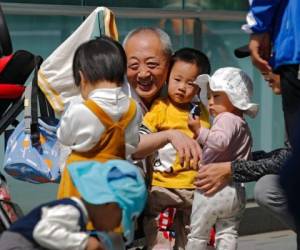 Un anciano juega con niños cerca de un edificio de oficinas en Beijing, el 10 de mayo de 2021. El gobierno chino relajará los límites de natalidad para permitir que todas las parejas puedan tener tres hijos en lugar de dos para hacer frente al rápido envejecimiento de la población, según dijo el lunes 31 de mayo una agencia estatal de noticias. Foto: AP