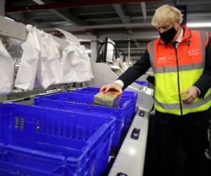 El primer ministro británico Boris Johnson coloca alimentos en canastas de plástico el miércoles 11 de noviembre de 2020 durante una visita a un centro de distribución en línea de los supermercados Tesco, en Londres.