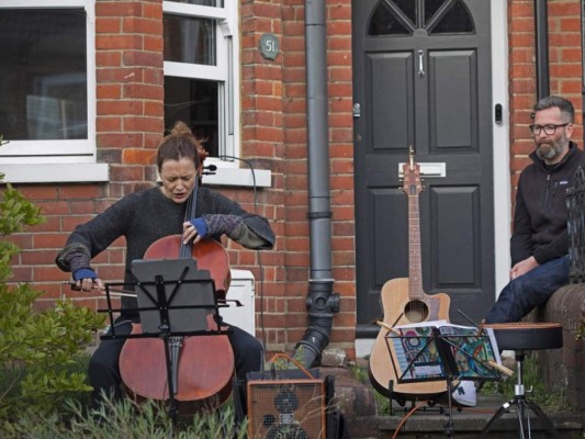 La concertista Clare O’Connell toca el cello ante la mirada de su esposo, el compositor Dom Shovelton, durante un concierto improvisado en la calle donde viven en Berkhamsted, Londres, el 2 de mayo del 2020, en plena pandemia por el coronavirus. Foto: Agencia AP.