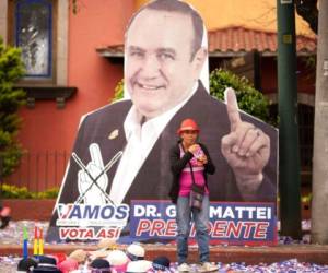 Un vendedor ambulante pone la mercancía en el suelo, frente a un recorte del candidato presidencial Alejandro Giammattei, del partido Vamos, cerca de su mitin de campaña en Ciudad de Guatemala. Foto: Agencia AP