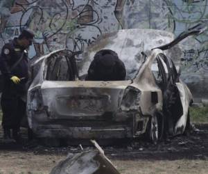 Policías revisan los restos de un coche bomba que explotó mientras las autoridades respondían a reportes de un vehículo con un cuerpo dentro en el barrio de San Bartolo, Soyapando, El Salvador. Agencia AP.