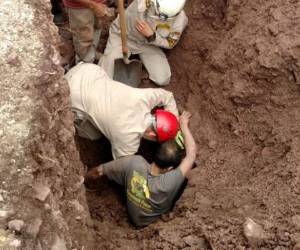 Dos elementos del Cuerpo de Bomberos de Honduras quitan la tierra que tiene atrapado la mitad del cuerpo del obrero. Foto Cortesía.