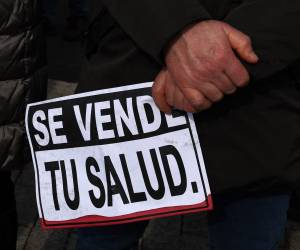 Una persona sostiene un cartel que dice “Tu salud en venta” durante una manifestación.