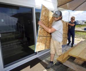 James Masog, al centro, y Gary Tavares, llevan una tabla de conglomerado para proteger las puertas de vidrio de la casa de un cliente en Charlestown, Rhode Island, antes de la llegada de Henri. Foto: AP.