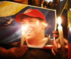 A supporter of Venezuelan President Hugo Chavez holds a poster of him and a candle outside the Venezuelan embassy in Quito on March 5, 2013, after knowing of his death. AFP PHOTO / RODRIGO BUENDIA