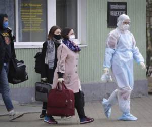 Una trabajadora sanitaria con un traje de protección acompaña a estudiantes hasta una ambulancia, en Minsk, Bielorrusia. Foto AP