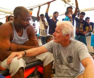 El actor Richard Gere, derecha, habla con migrantes al bordo del buque humanitario Open Arms durante el cruce del Mediterráneo, viernes 9 de agosto de 2019. (AP Foto/Valerio Nicolosi)