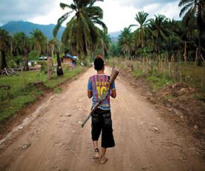 In this May 5, 2012 photo, Enrique Martinez, 17, with a rifle slung over his back, patrols an area of La Confianza, Honduras, a city developed from land seized by small-scale farmers from one of Honduras' richest men. The collection of tin-and-wood shacks boasts a health center, a school, a meeting hall, and a store. The land seizure has spawned a violent land conflict between the farmers and owner, billionaire Miguel Facusse, that has killed at least 63 people, mostly peasants, in the last three years in the Bajo Aguan Valley. (AP Photo/Rodrigo Abd)