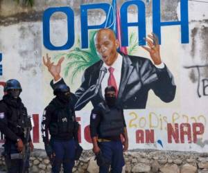 Agentes policiales vigilan una calle en la capital haitiana, mientras a sus espaldas se observa una pintura en honor a Jovenel Moise, presidente asesinado. Foto: AFP