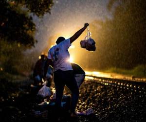 Los migrantes se inclinan peligrosamente tratando de atrapar al vuelo una de las bolsas de comida. Algunos incluso bajan del tren y corren a su lado mientras recogen su botín. Foto: Agencia AFP