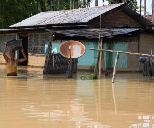Un hombre lleva sus pertenencias a través de un área inundada después de fuertes lluvias en el distrito de Morigaon del estado indio de Assam el 22 de mayo de 2022.