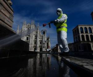 Un empleado con equipo de protección, que trabaja para la empresa de servicios ambientales AMSA, rocía desinfectante en la Piazza Duomo de Milán. Foto AFP