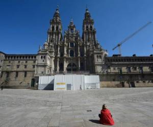 A woman sits outside the Santiago de Compostela Cathedral in the usually overcrowded Obradoiro Square in Santiago de Compostela on March 14, 2020 after regional authorities ordered all shops in the region be shuttered from today through March 26, save for those selling food, chemists and petrol stations, in order to slow the coronavirus spread. (Photo by MIGUEL RIOPA / AFP)